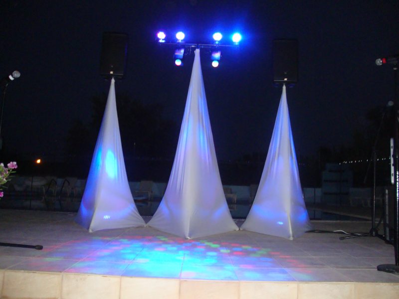 Speakers on stands with covers and uplighters and a large T b-bar with spotlights and effects